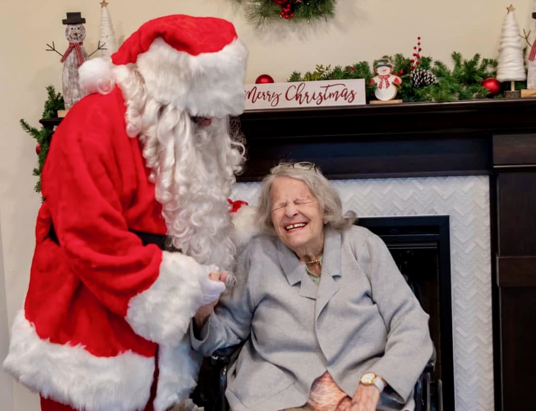 Santa Suscheck laughing with a senior center resident seated by the fireplace